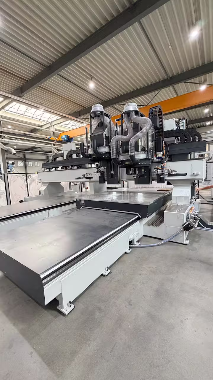 Freie Gesamtansicht einer großen weißen CNC-Portalfräsmaschine mit zwei Bearbeitungsköpfen, Absaugschläuchen und langem Maschinentisch in einer Industriehalle