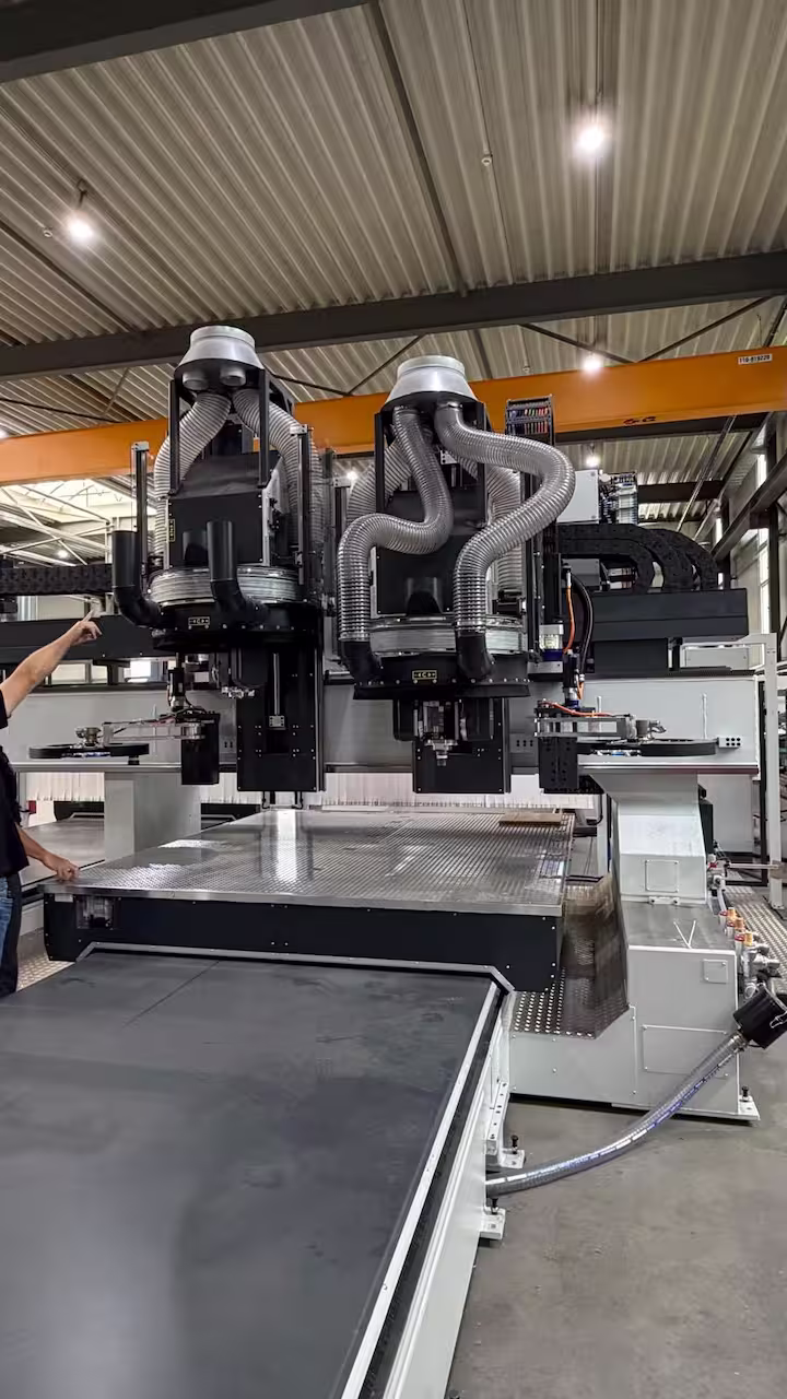 Nahaufnahme einer modernen CNC-Portalfräsmaschine mit zwei Fräsköpfen, silbernen Absaugschläuchen und Teller-Werkzeugwechslern