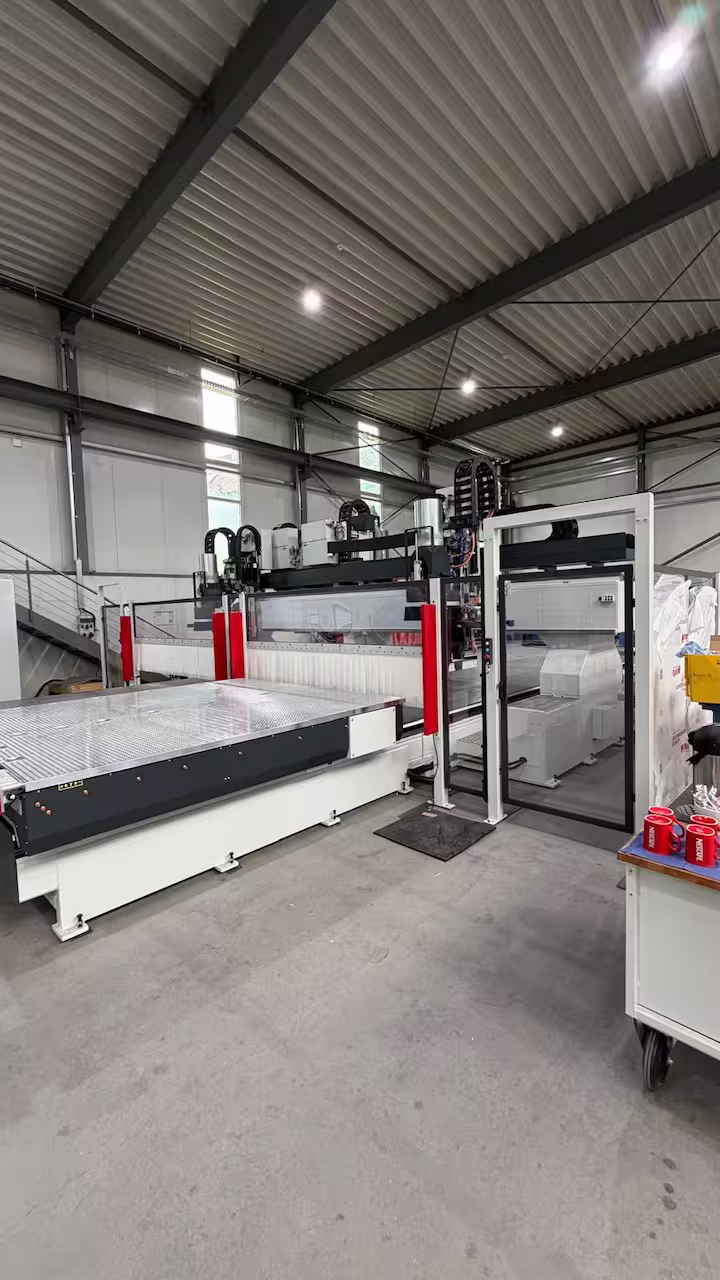 CNC-Portalfräsmaschine mit Riffelblech-Vakuumtisch, Schutzumhausung und Werkstattwagen mit roten Tassen im Vordergrund
