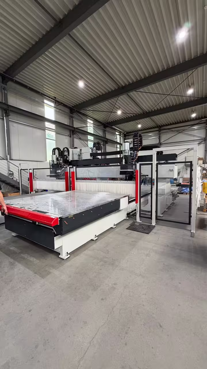 Moderne weiße CNC-Portalfräsmaschine mit großem silbernen Vakuumtisch, roter Schutzkante und Sicherheitseinhausung in einer hellen Fertigungshalle.