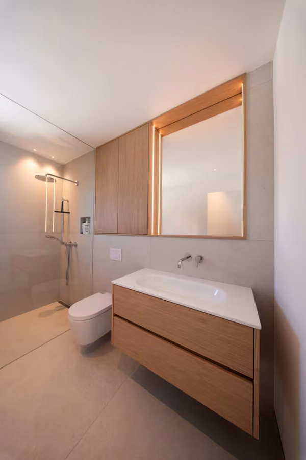 Badezimmer mit Waschtischunterschrank in Holzoptik, Spiegelschrank mit Holzrahmen und Wand-WC.