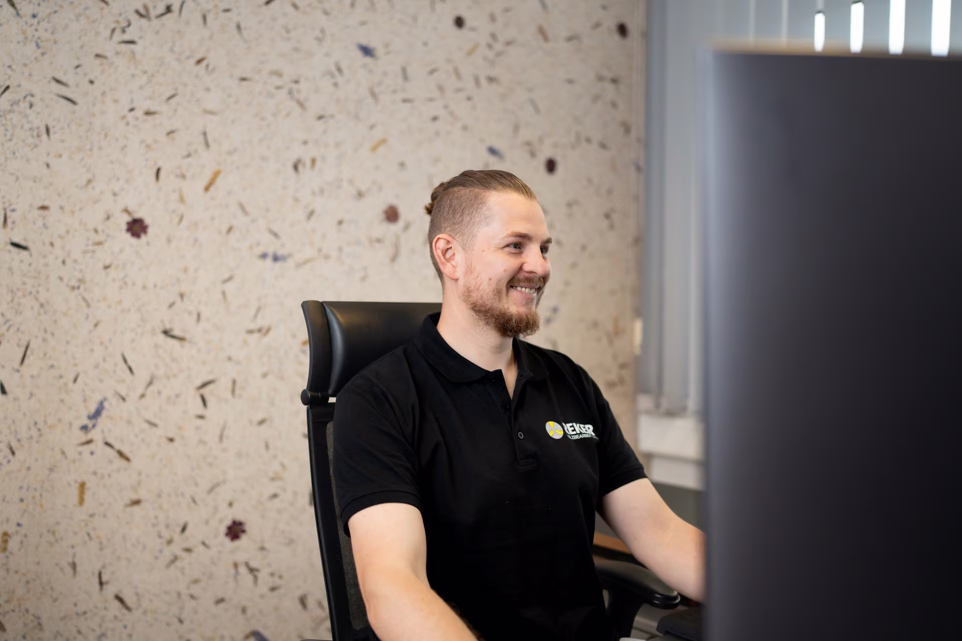 Lächelnder Mitarbeiter sitzt an seinem Büroarbeitsplatz vor einem Monitor.