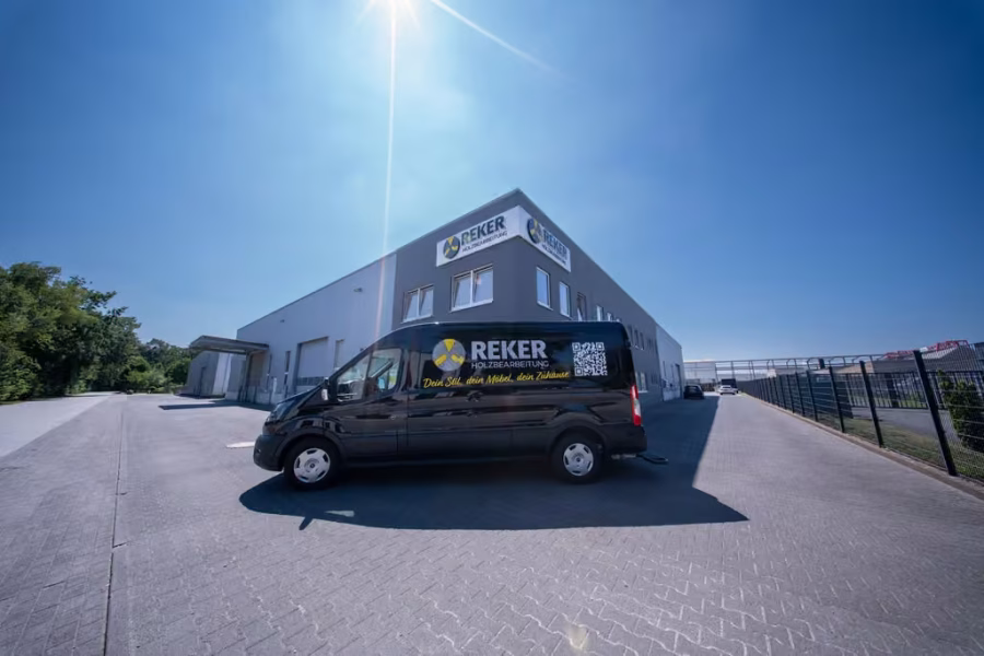 Schwarzer Transporter mit Reker-Logo vor dem Firmengebäude unter blauem Himmel.