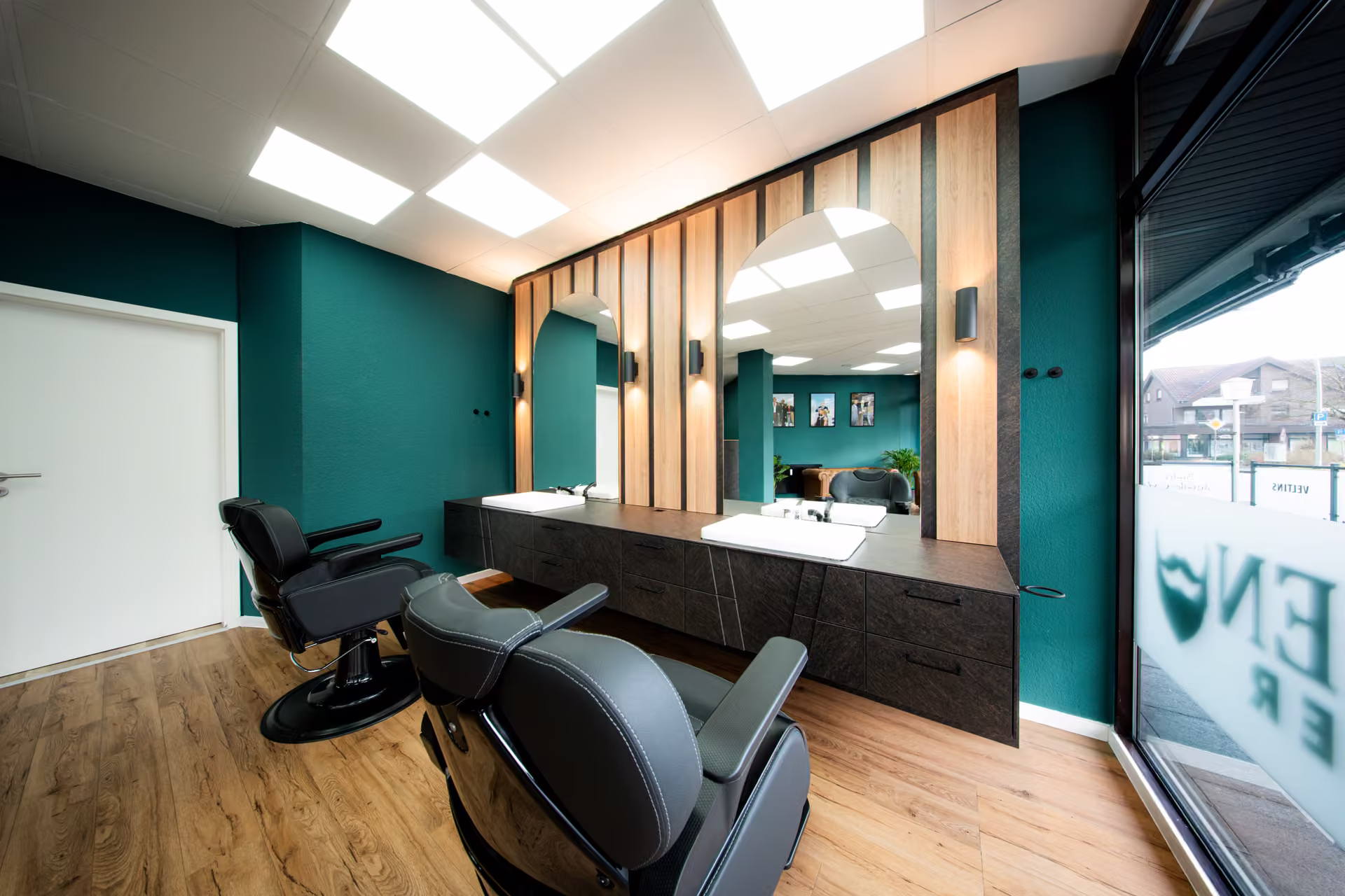 Friseursalon mit petrolfarbener Wand, Holzlamellen, Spiegelplätzen und schwarzen Friseurstühlen.