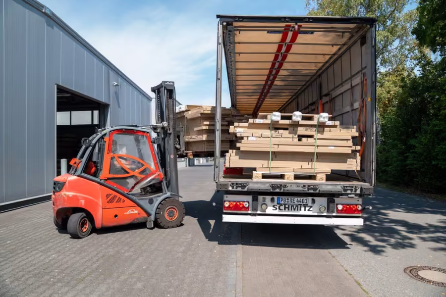 Roter Gabelstapler belädt einen LKW mit Plattenpaketen an der Hallenrampe.