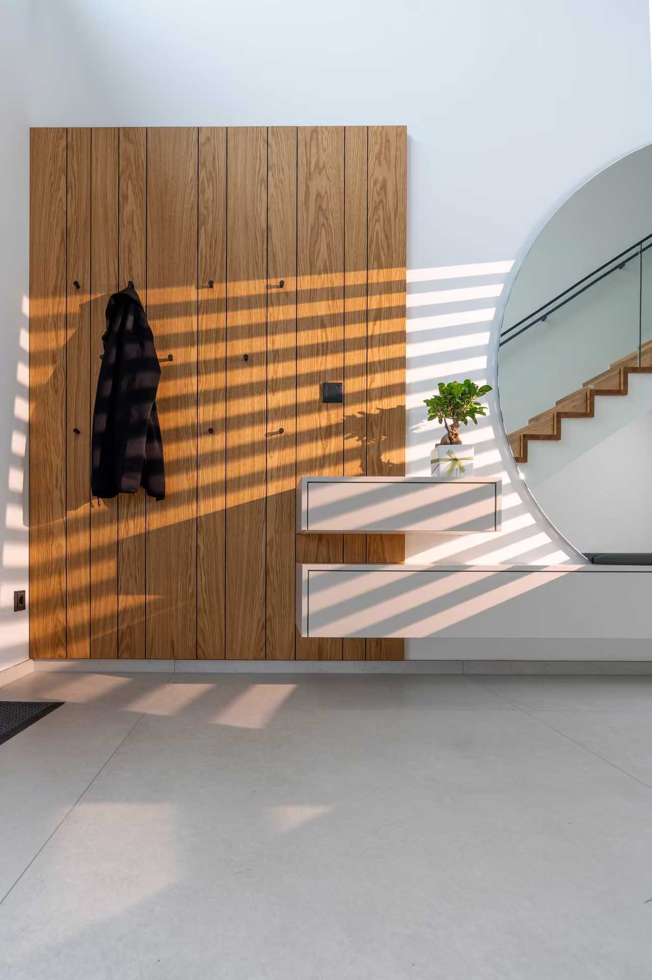 Garderobe im Flur mit Holzpaneel, Wandhaken, Jacke, Ablage und rundem Spiegel neben der Treppe.