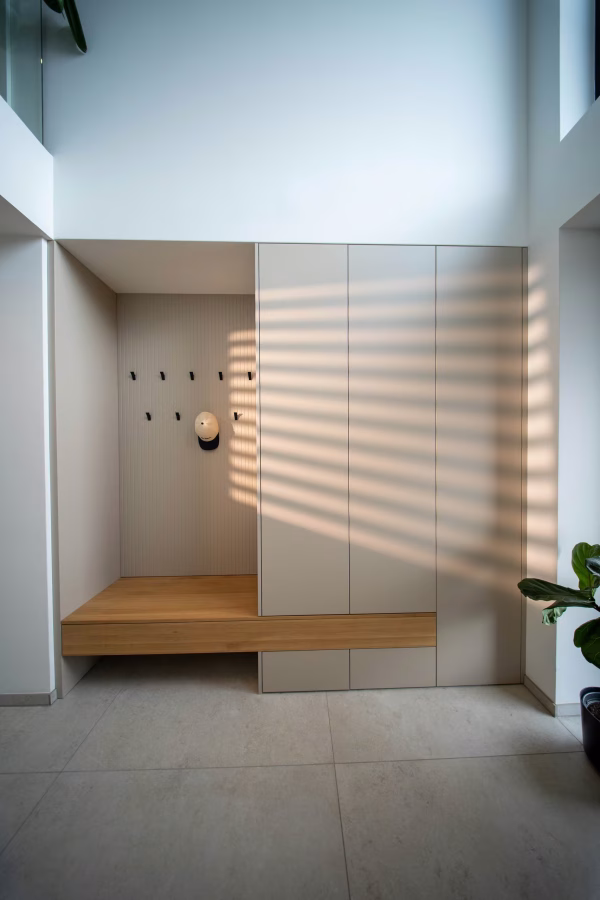 Frontalansicht einer Garderobennische mit Holz-Sitzbank, Wandhaken und angrenzendem Einbauschrank.