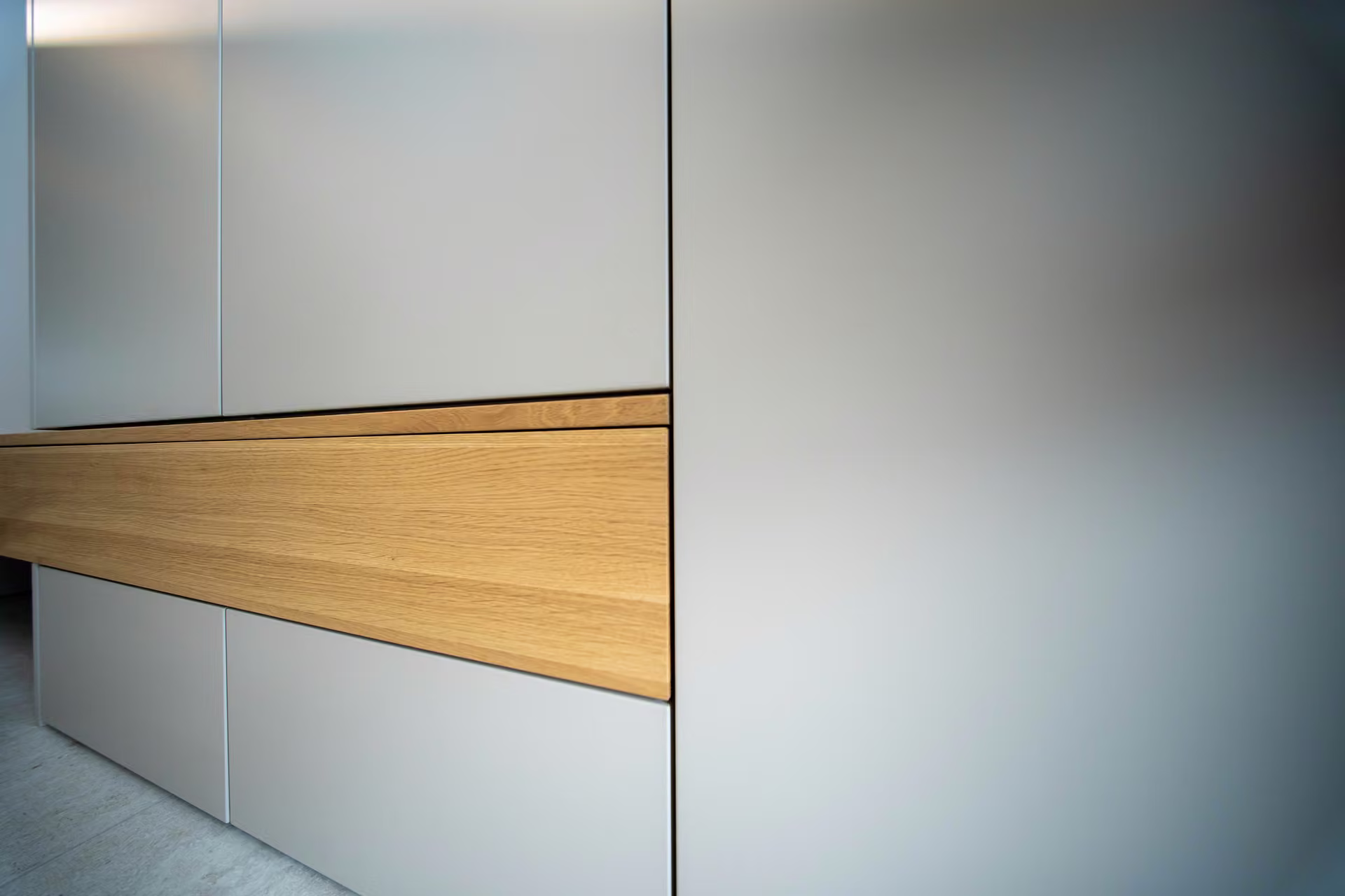 Detailaufnahme einer hellgrauen Schrankfront mit eingesetzter Holzleiste.