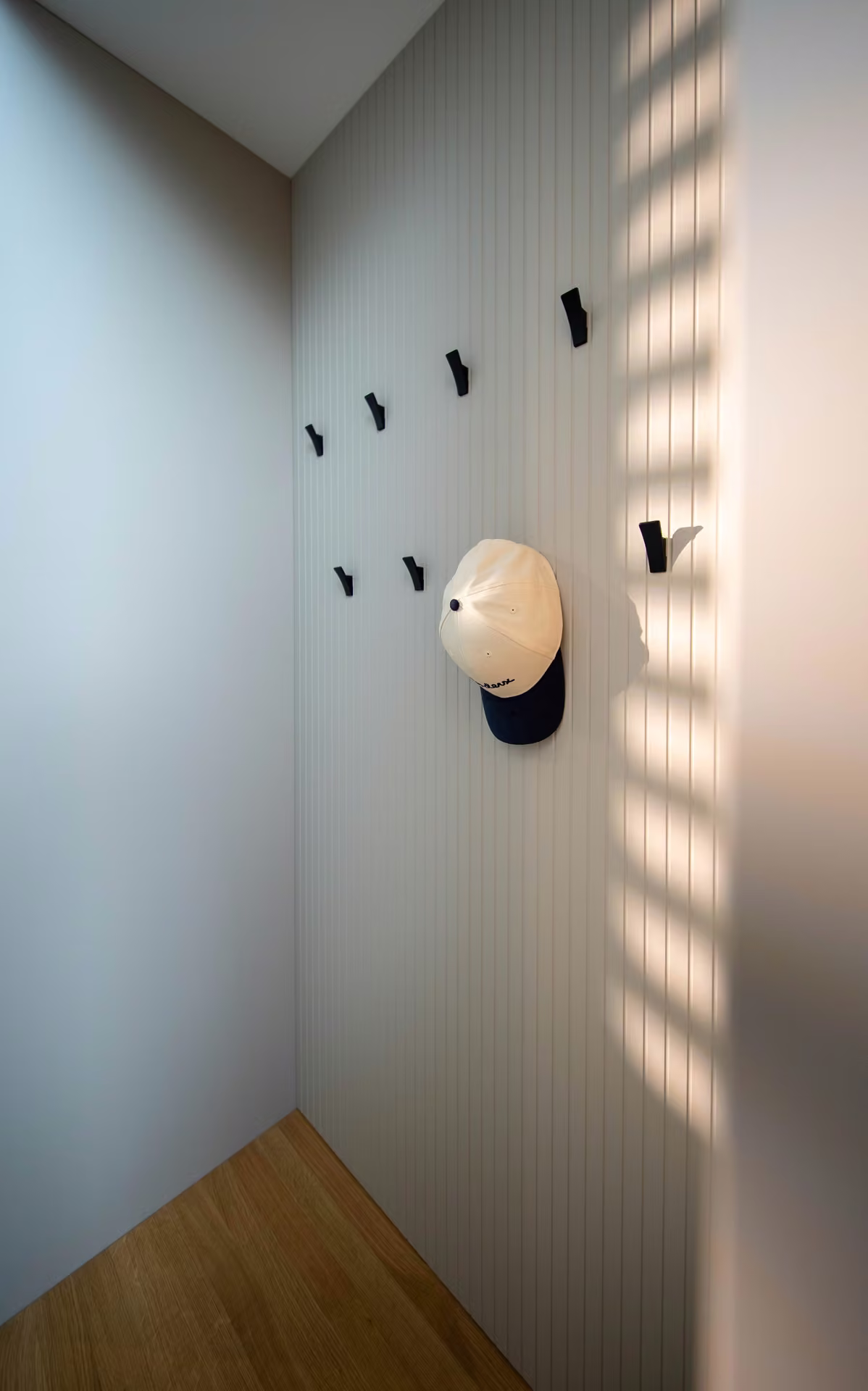 Schwarze Wandhaken und ein Hut an der Wand einer Garderobennische mit Sonnenstreifen.