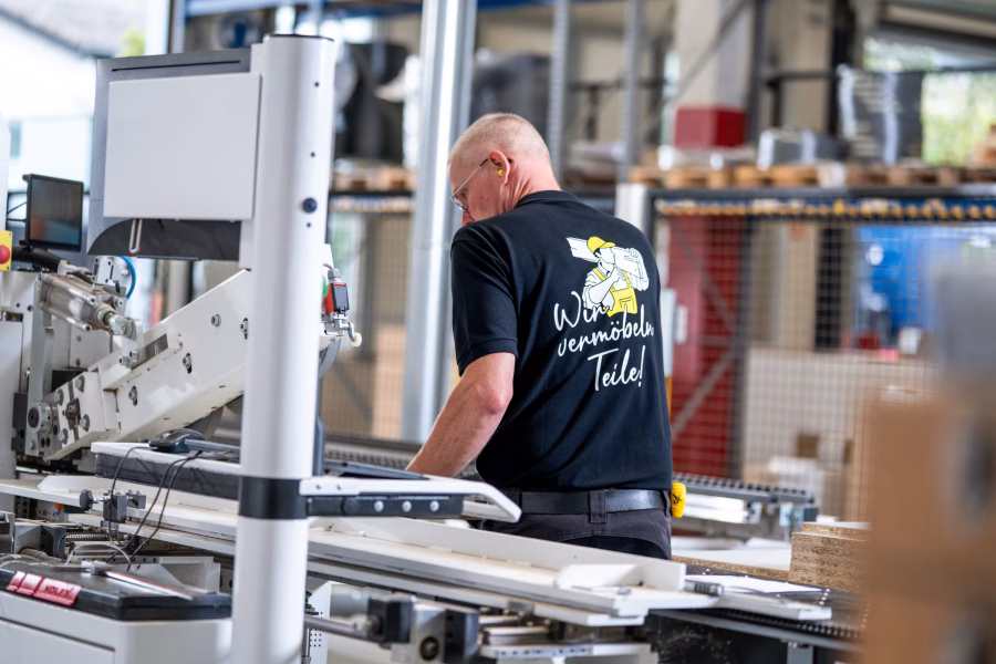 Mitarbeiter von hinten am Bedienterminal einer Kantenanleimmaschine in der Werkhalle.