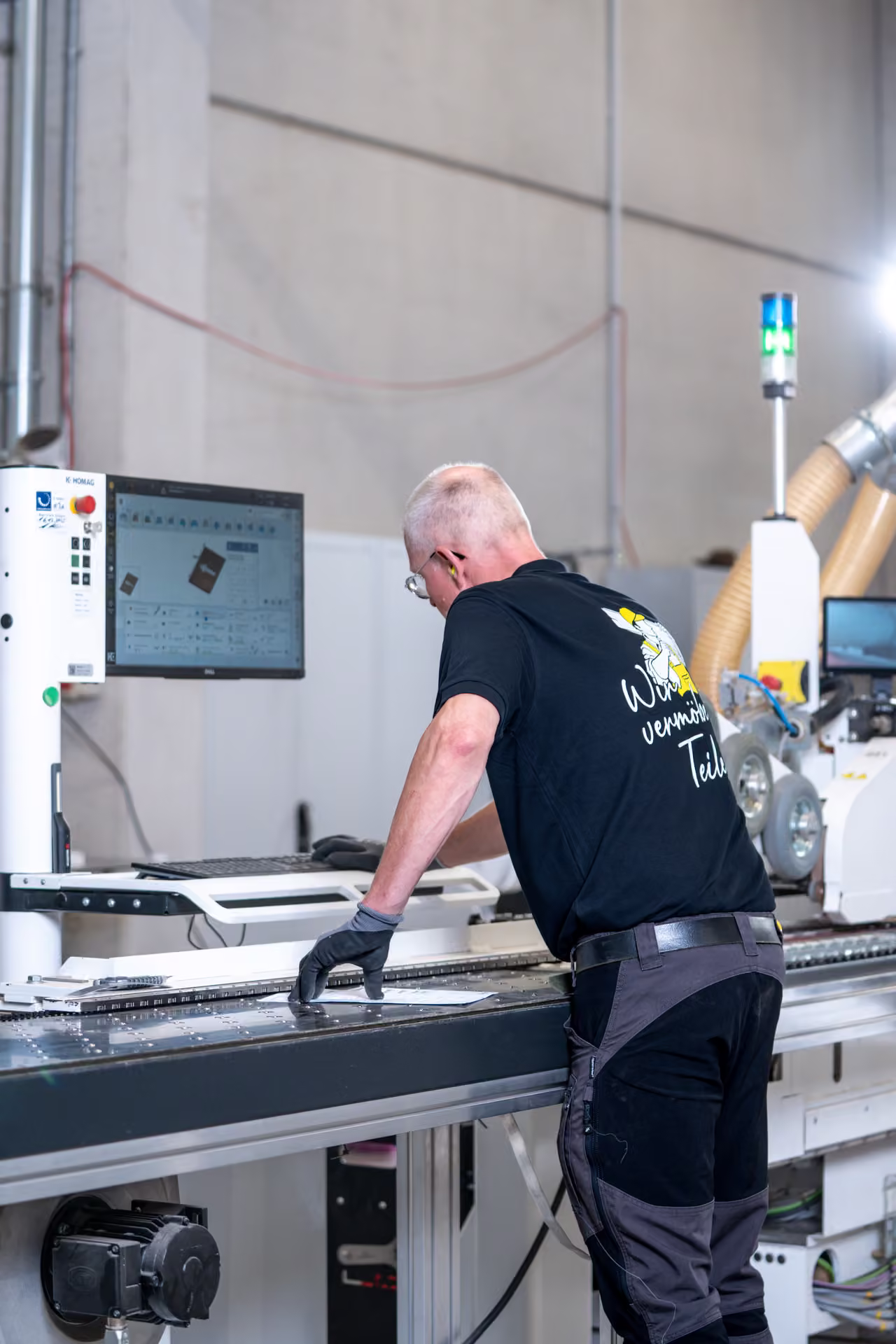 Mitarbeiter mit Handschuhen bedient die Steuerung der Kantenanleimmaschine, Hochformat.