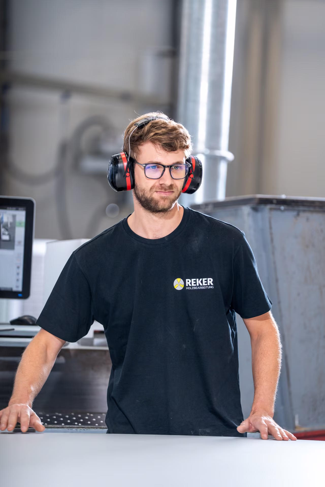 Mitarbeiter mit Brille und Gehörschutz steht frontal an einem Maschinentisch in der Produktion.