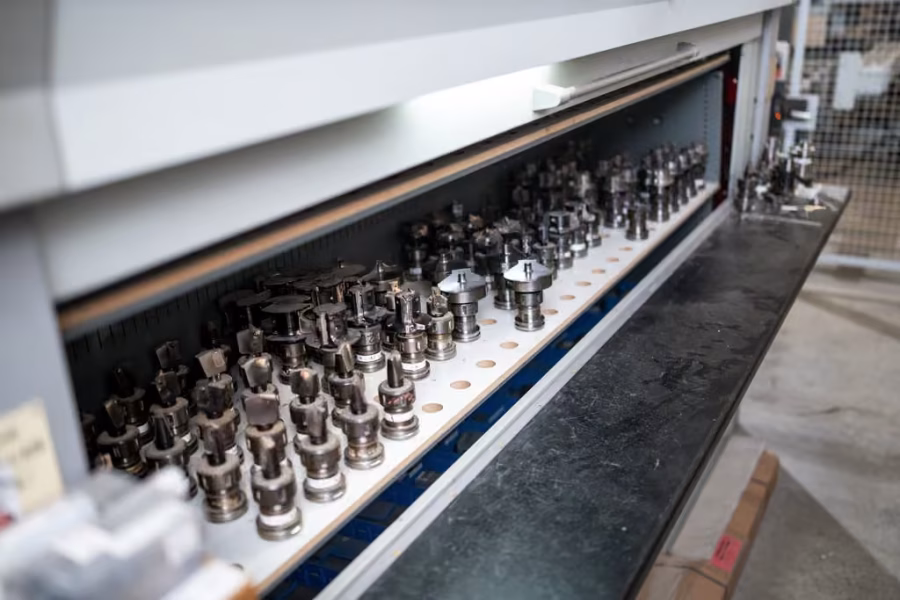 Lange Reihe von Werkzeugaufnahmen mit Fräsern in einem beleuchteten Werkzeugschrank.