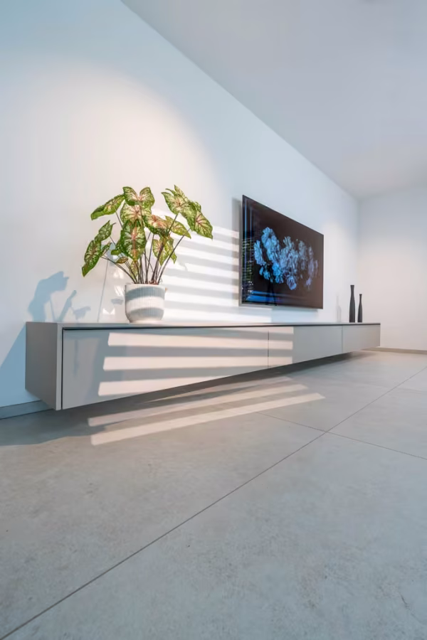 Wandhängendes graues Lowboard im Wohnzimmer mit Pflanze und Fernseher an der Wand.
